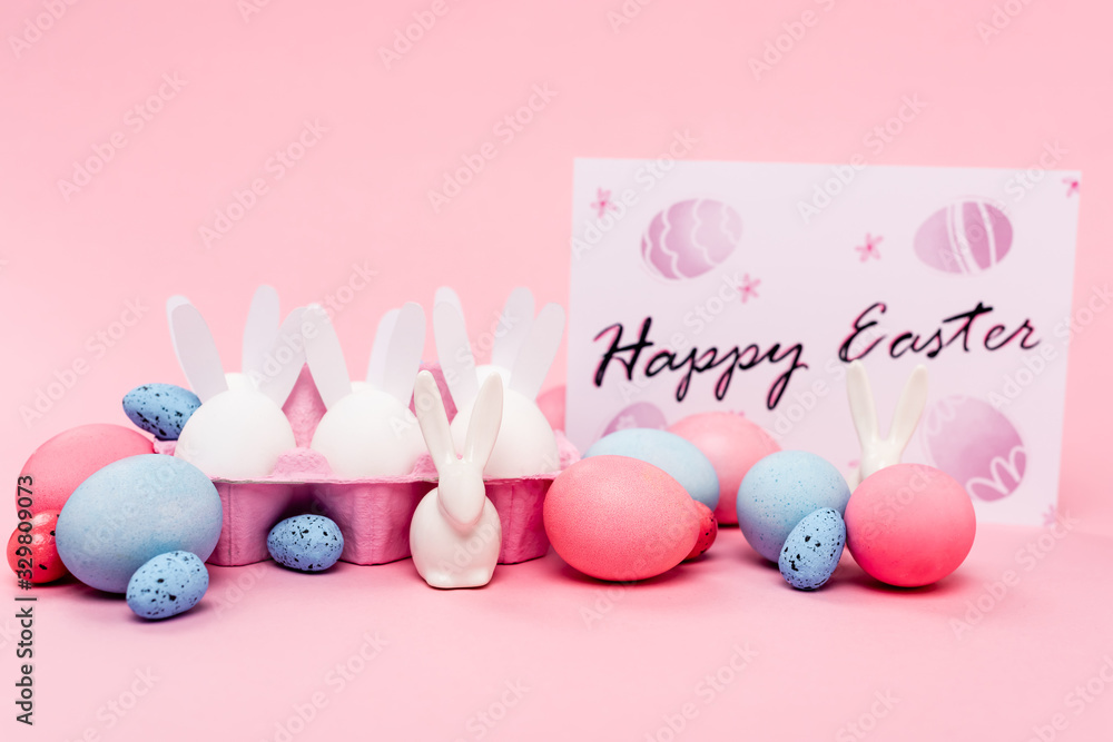 Colorful eggs, decorative bunnies and card with happy easter lettering on pink