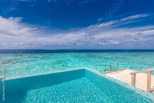 Fototapeta Naklejka Na Ścianę i Meble -  Minimalist infinity pool in tropical paradise beach. Luxury resort travel background. Blue sea view with calming sky and clouds. Beautiful tropical island. Swimming pool ladder, tranquil exotic view