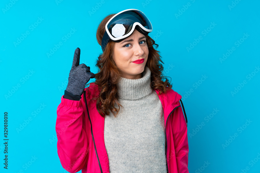 Skier woman with snowboarding glasses over isolated blue wall pointing with the index finger a great idea Skier woman with snowboarding glasses over isolated blue wall pointing with the index finger a great idea
