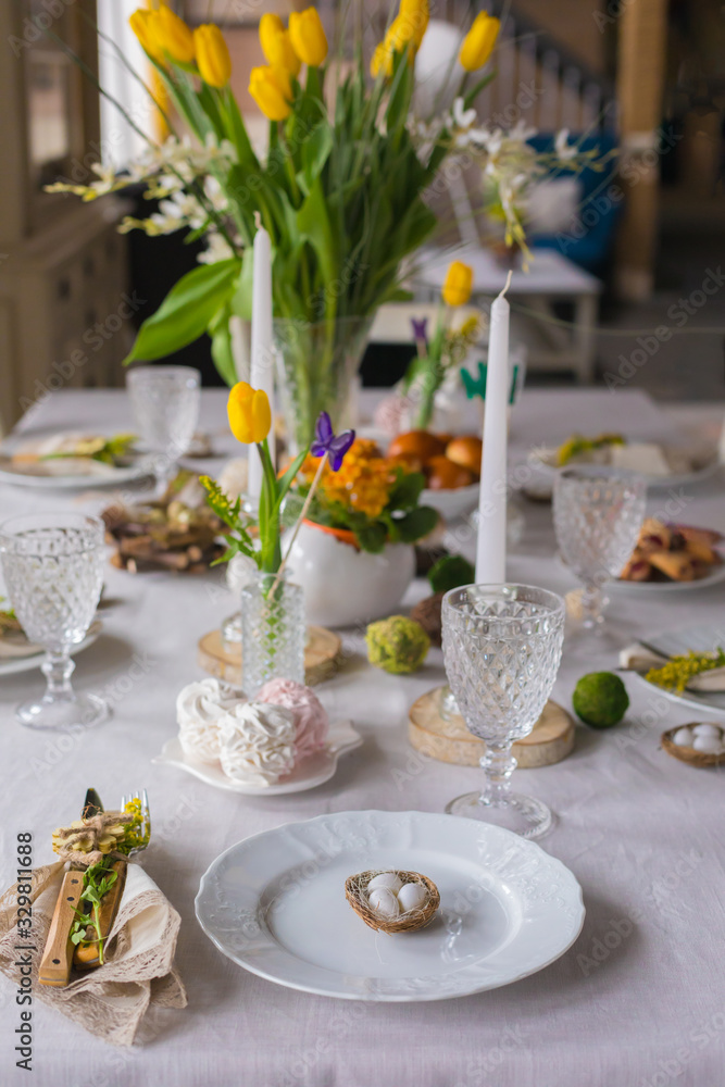 Easter festive spring table setting decoration, eggs in nest, fresh yellow tulips, marshmallows, selective focus