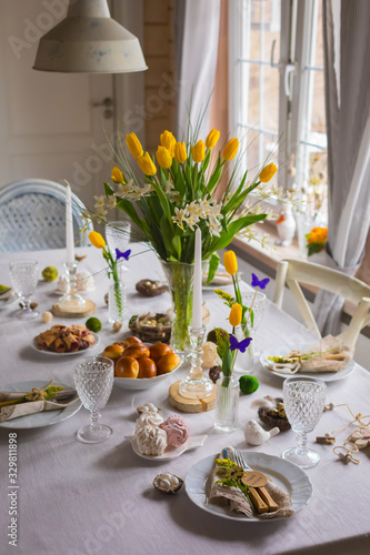 Easter festive spring table setting decoration, eggs in nest, fresh yellow tulips, marshmallows, selective focus
