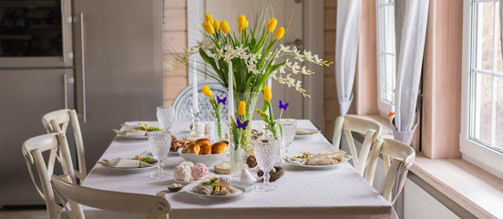 Easter festive spring table setting decoration, eggs in nest, fresh yellow tulips, marshmallows, selective focus banner