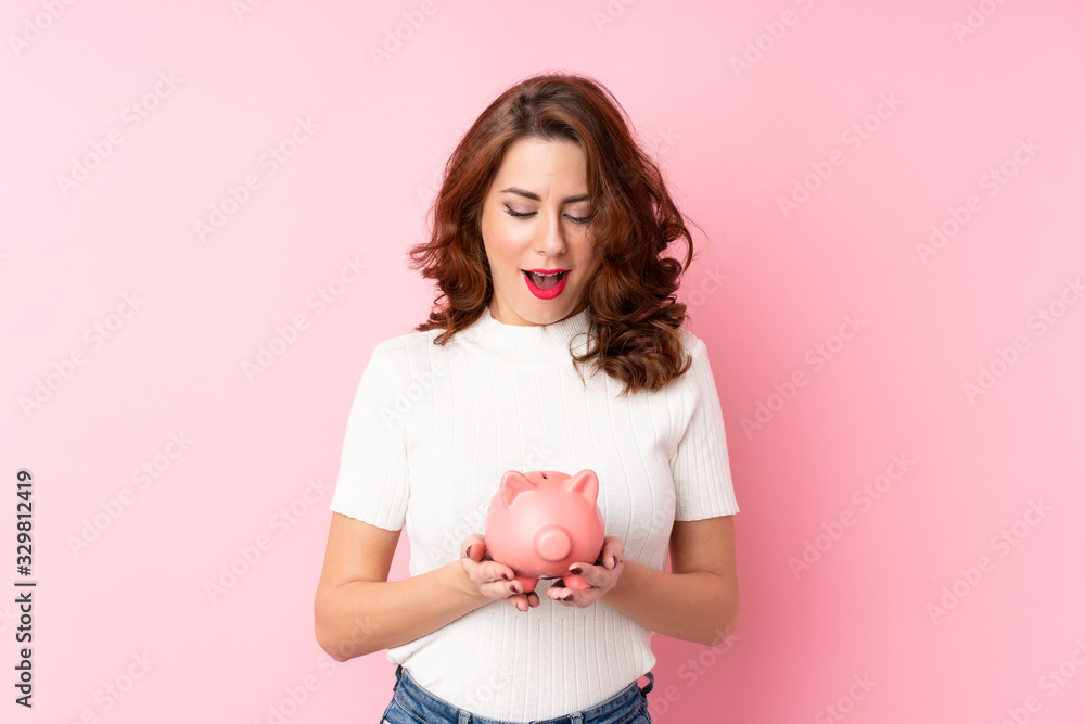 Young Russian woman over isolated pink background holding a big piggybank Young Russian woman over isolated pink background holding a big piggybank