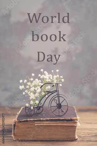 Old book, iron bicycle with flowers on wooden background, World Book Day concept, toned vintage, selective focus