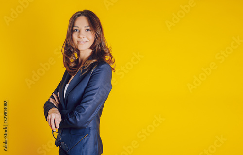 A beautiful young woman dressed elegantly as a teacher, like a bissnes lady, smiling and well placed on a yellow background