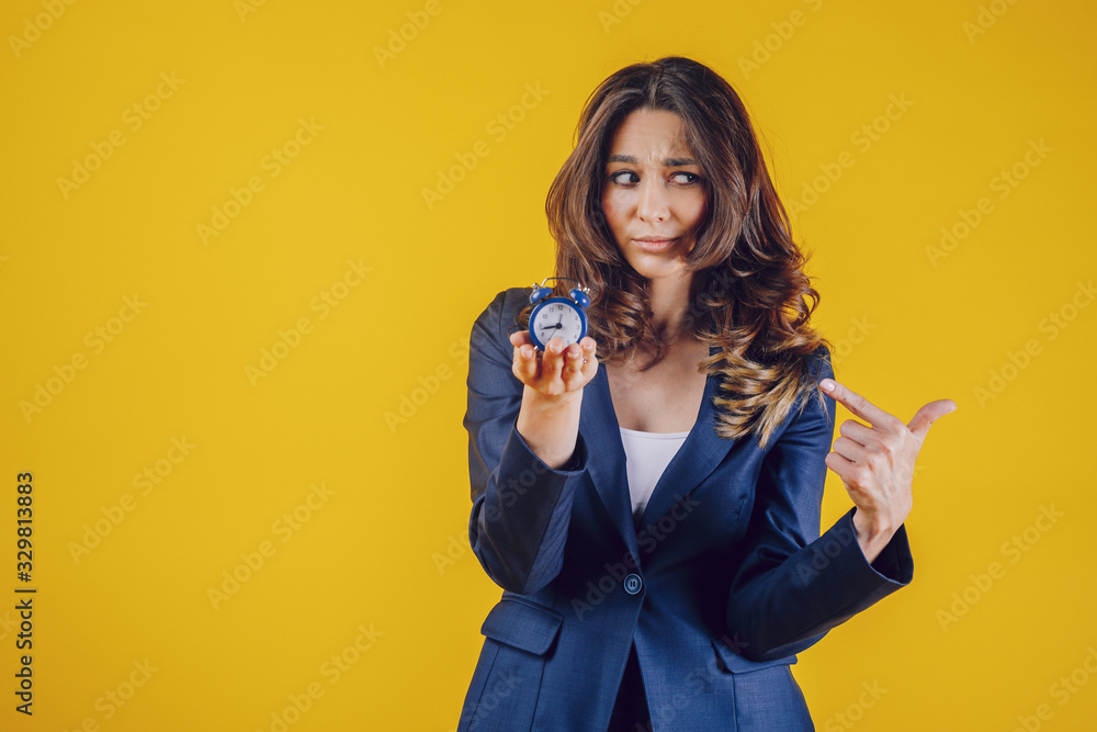 The American woman dressed elegantly as a teacher or business lady, holds a watch in her palm and points her finger at him, feels tired and cramped and sad. The American woman dressed elegantly as a teacher or business lady, holds a watch in her palm and points her finger at him, feels tired and cramped and sad.