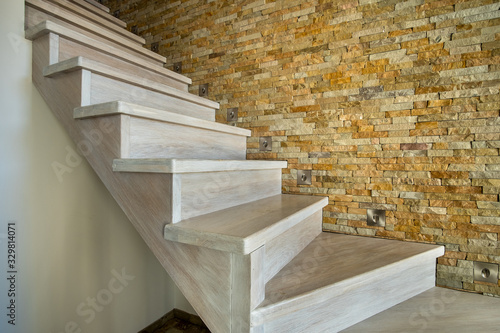 Stylish wooden contemporary staircase inside loft house interior. Modern hallway with decorative limestone brick walls and white oak stairs.