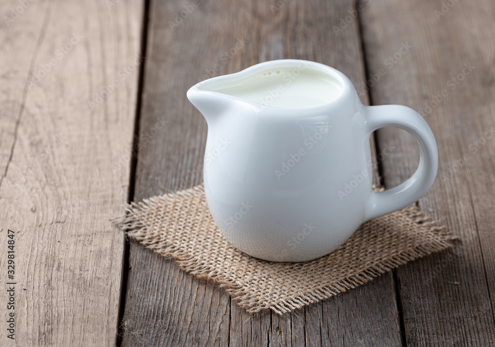 White jug with milk on a wooden rustic background White jug with milk on a wooden rustic background