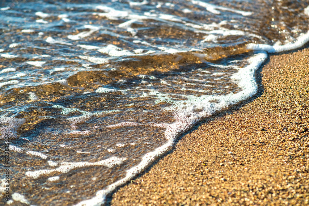 Close up of small sea waves with clear blue water over yellow sand beach at summer sunny shore.