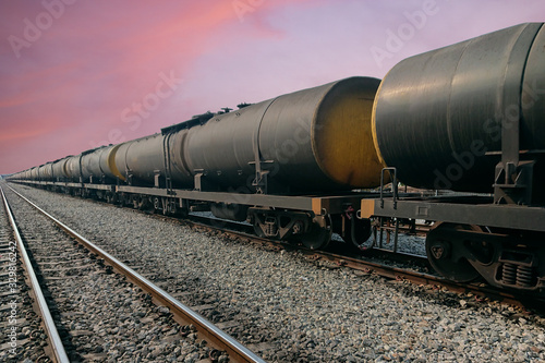 Black freight train wagons having oil tankers waiting on the rails againt sunrise sky