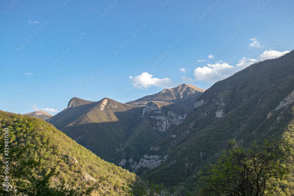 Mountains landscape, sunny day. White clouds on a blue sky. The mountains are covered with green vegetation.