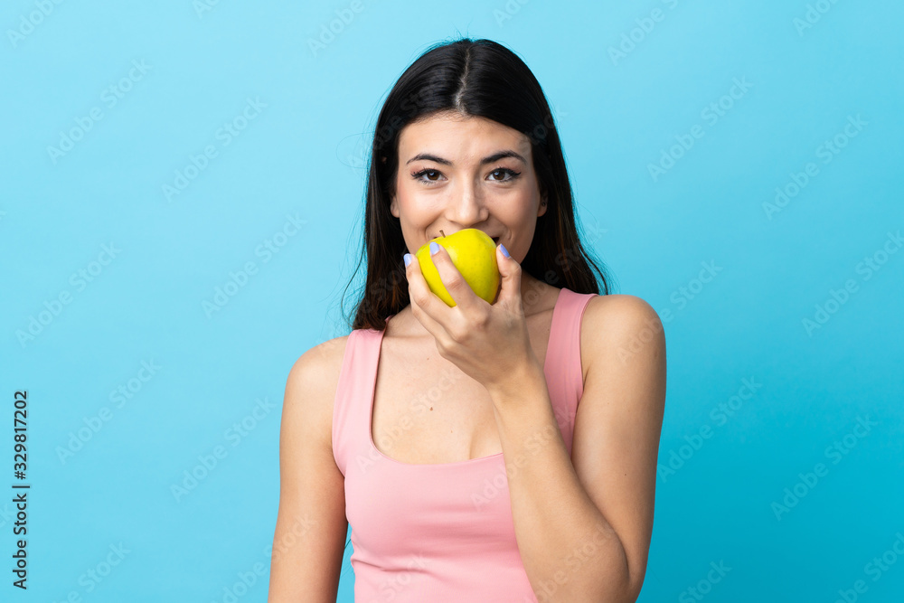 Young brunette girl over isolated blue background eating an apple Young brunette girl over isolated blue background eating an apple