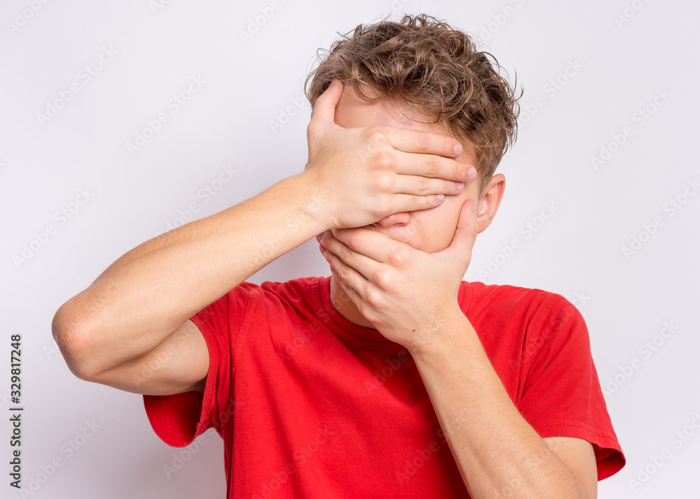 Portrait of teen boy with hands on face covering eyes and mouth. Beautiful teenager close face with palms. Funny child on gray background shows surprised or shocked, sad or happy - hiding emotion. Portrait of teen boy with hands on face covering eyes and mouth. Beautiful teenager close face with palms. Funny child on gray background shows surprised or shocked, sad or happy - hiding emotion.