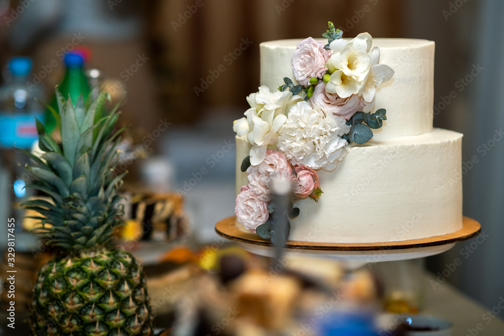 Tall sweet wedding cake decorated with live pink and white flowers on a table.