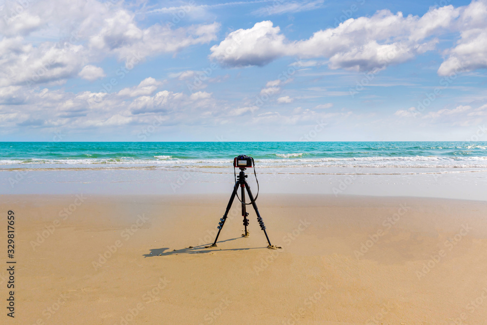 Digital professional camera stand on tripod photographing sea.