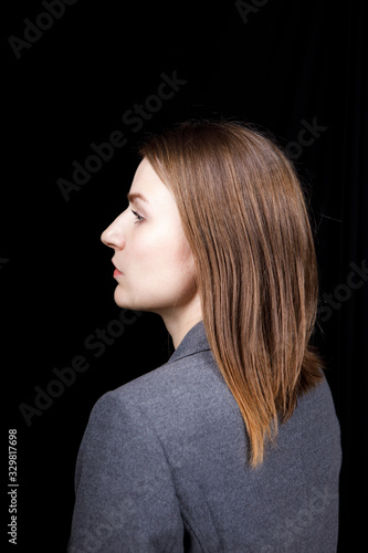 A cute woman with clean skin in a grey business jacket turned in profile on black background