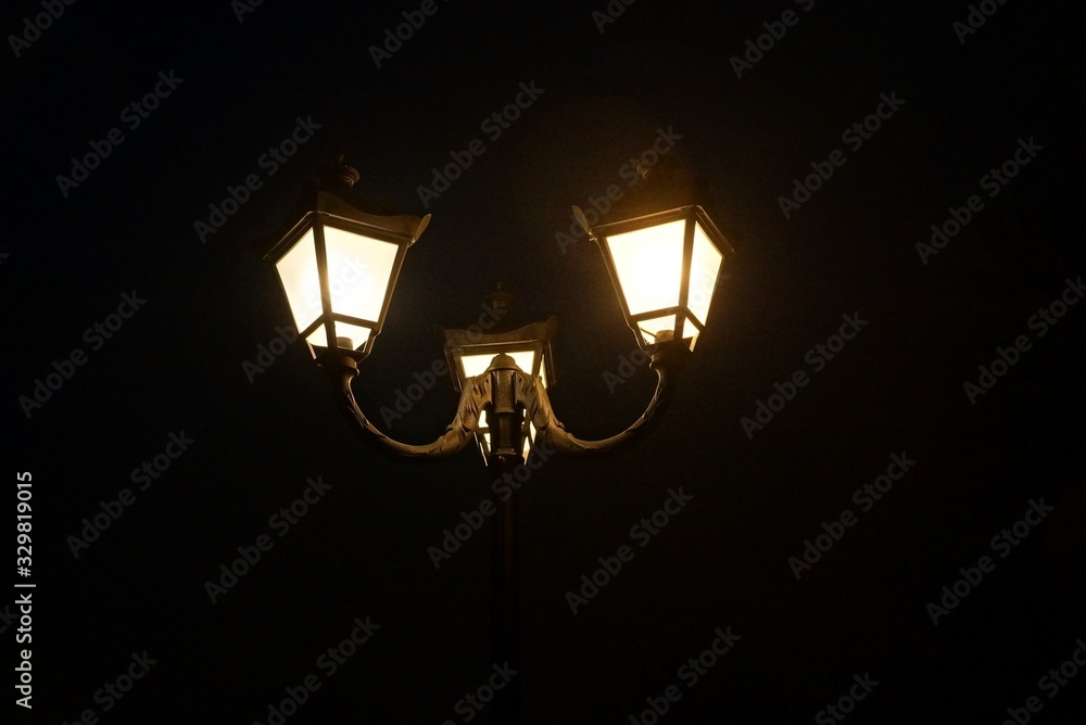 three lanterns on a pole with white glow on a black background of a night street