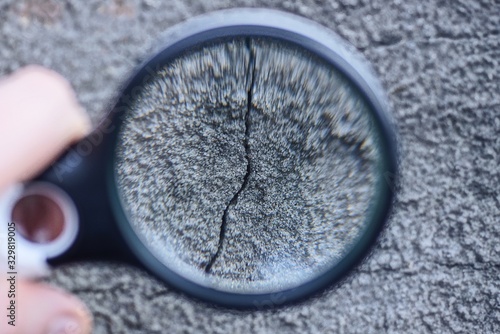 magnifier in hand enlarges black crack on gray concrete wall photo