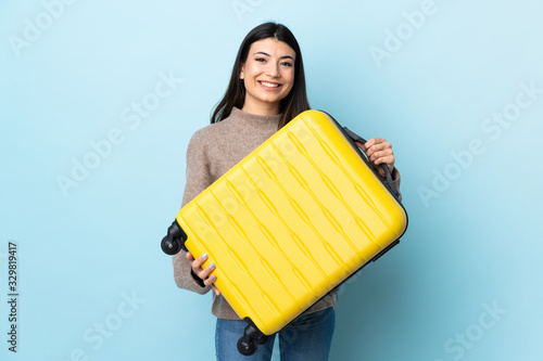 Young brunette girl over isolated blue background in vacation with travel suitcase