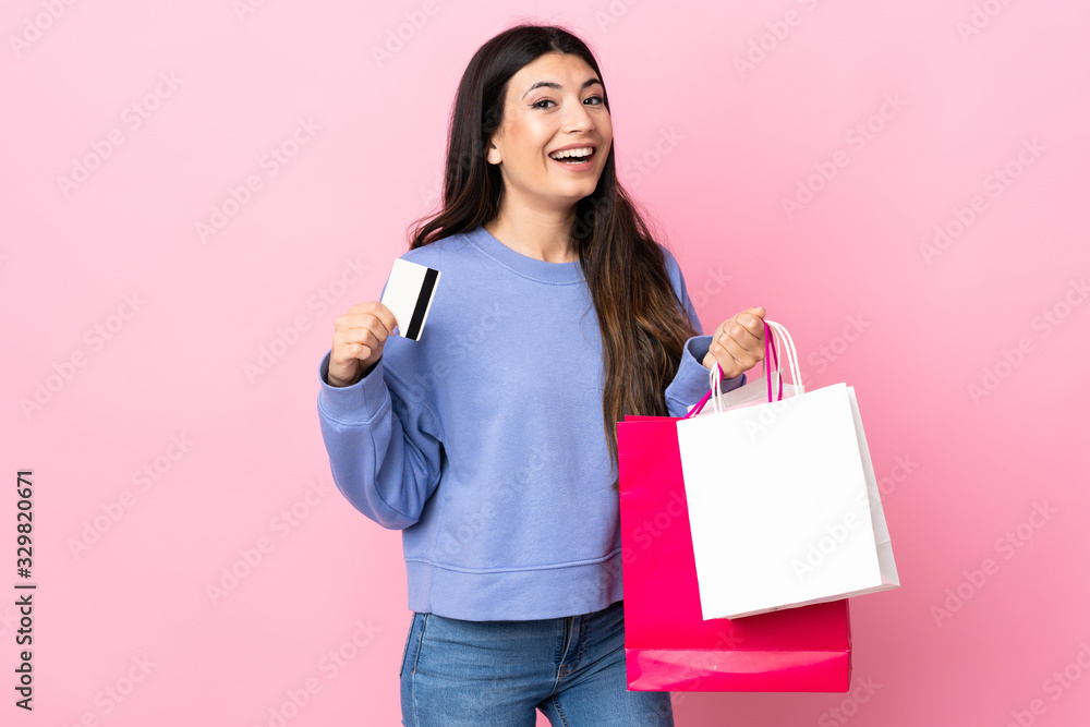 Young brunette girl over isolated pink background holding shopping bags and a credit card Young brunette girl over isolated pink background holding shopping bags and a credit card