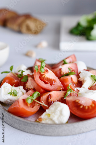 Italian Сaprese salad with sliced tomatoes, mozzarella cheese, basil, olive oil in a plate on grey concrete table. Selective focus
