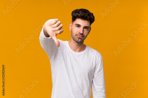 Young man over isolated orange background showing thumb down with negative expression