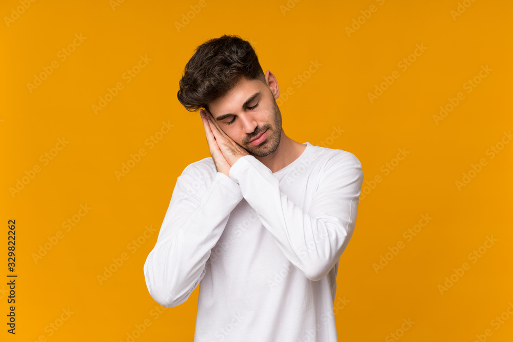 Young man over isolated orange background making sleep gesture in dorable expression Young man over isolated orange background making sleep gesture in dorable expression