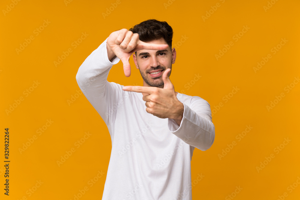 Young man over isolated orange background focusing face. Framing symbol Young man over isolated orange background focusing face. Framing symbol