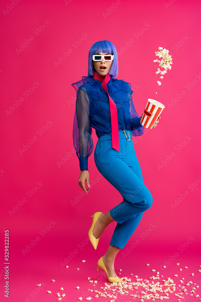 surprised pop art girl in purple wig and 3d glasses throwing popcorn, on pink