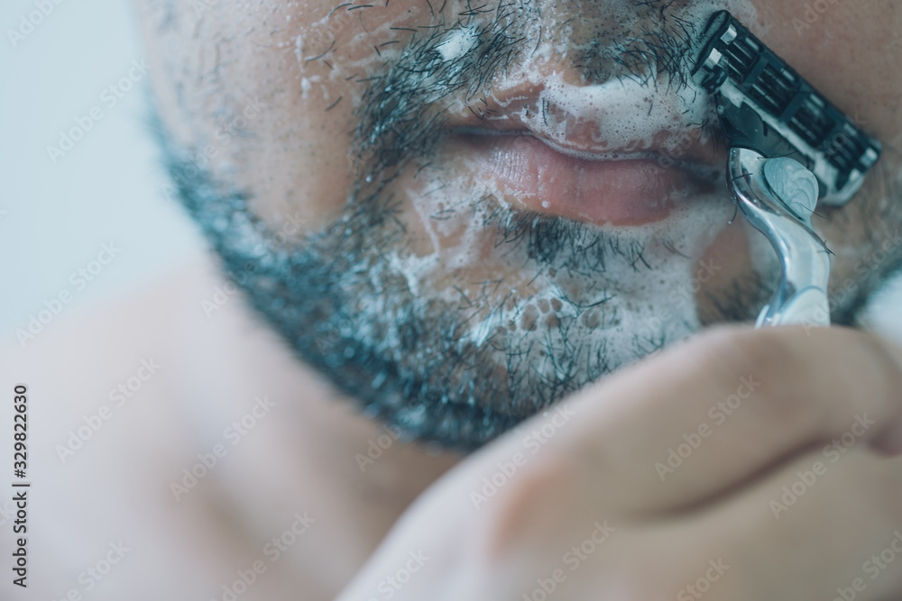 Fototapeta premium Man is shaving beard his face in bathroom in morning.