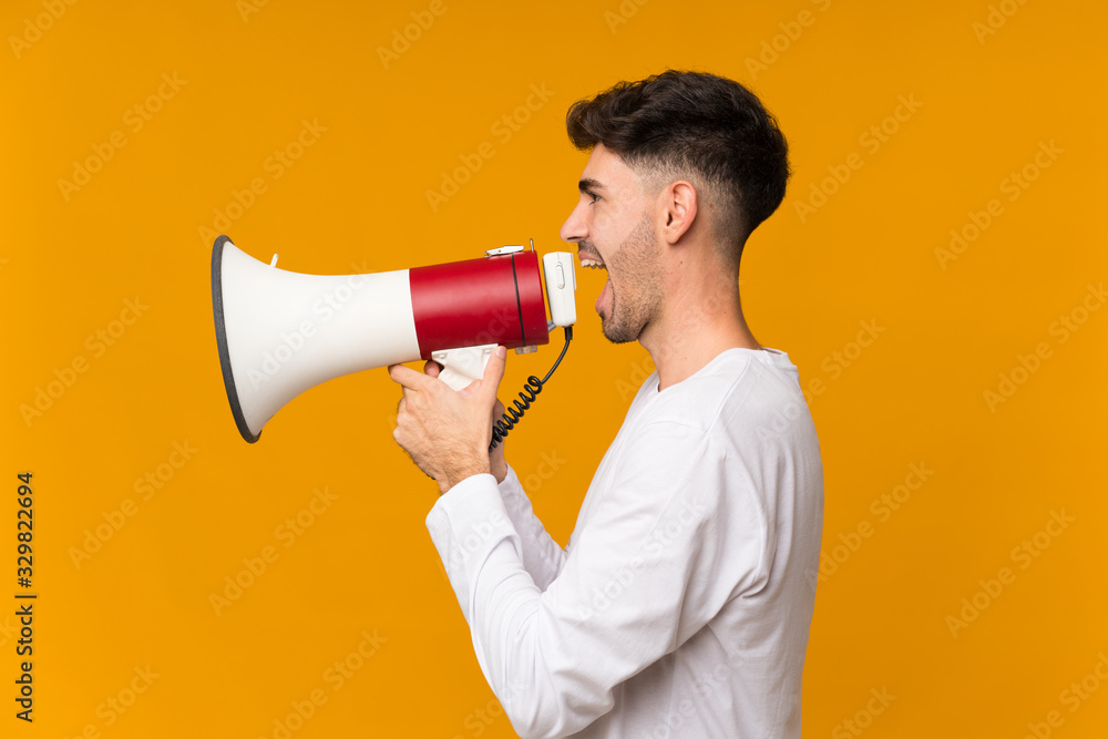 Young man over isolated orange background shouting through a megaphone Young man over isolated orange background shouting through a megaphone