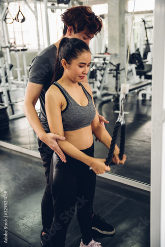 Attractive woman doing exercise with personal trainer at gym.