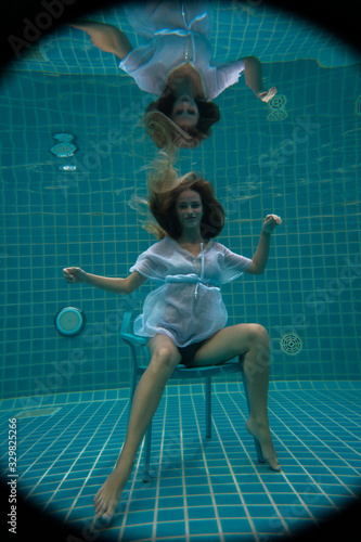 Beautiful woman with long red hair posing underwater on the chair