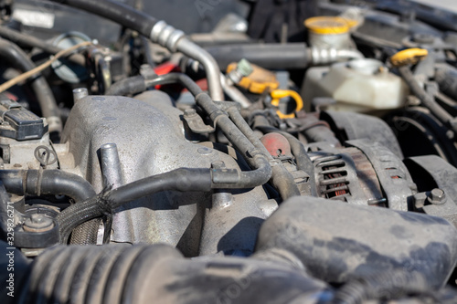 Dusty details of a flat-four (boxer) car engine compartment under the open hood. Alternator and intake manifold. Closeup side view on a sunny day. Selective focus