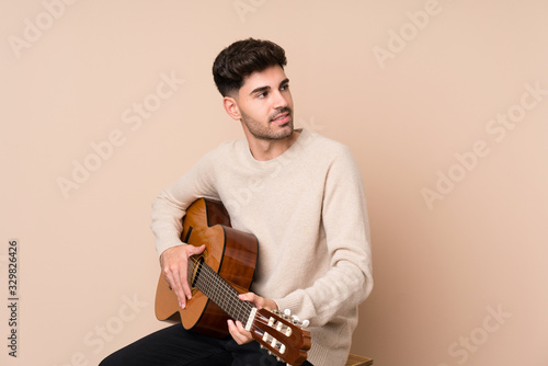 Young man with guitar over isolated background looking side