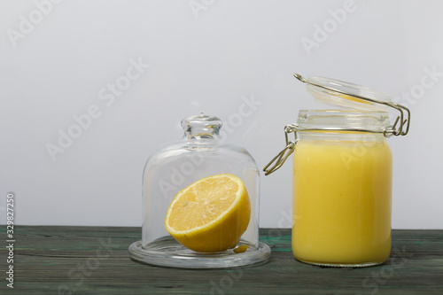 Lemon Kurd in a glass jar. Nearby is half a lemon in a container with a glass lid. Stand on brushed boards, on a white background.