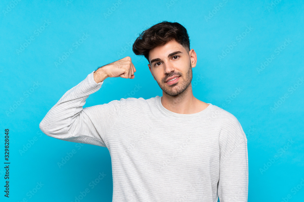 Young man over isolated blue background doing strong gesture Young man over isolated blue background doing strong gesture