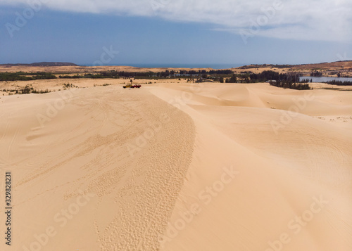 Aerial view of brown winding sand dunes with four-wheel car