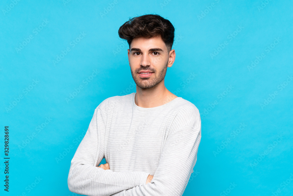 Young man over isolated blue background with arms crossed and looking forward Young man over isolated blue background with arms crossed and looking forward