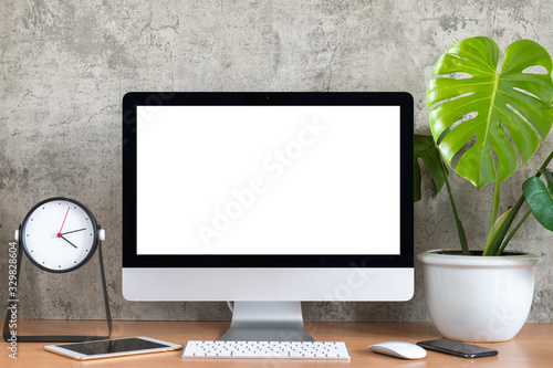Blank screen of All in one computer, keyboard, mouse, tablet, smart phone, monstera plant pot and clock on wooden table