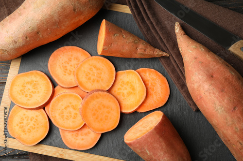 Sweet potato, board and towel on wooden background, top view