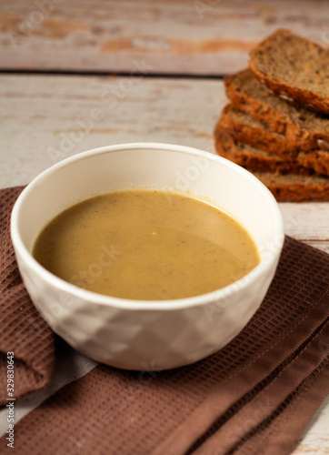 Hot tasty mushroom cream soup in a white bowl on a brown kitchen towel with bread background