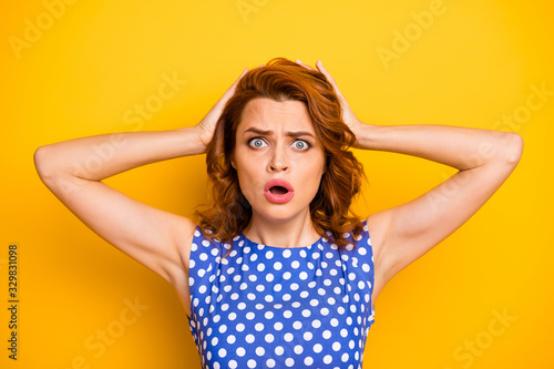 Closeup photo of terrified pretty wavy ginger lady holding arms on head open mouth listen terrible news wear retro style dotted blue white shirt isolated yellow color background