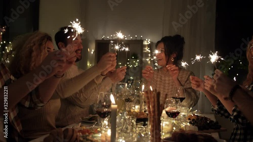 holidays, celebration and people concept - happy friends with sparklers having christmas dinner at home