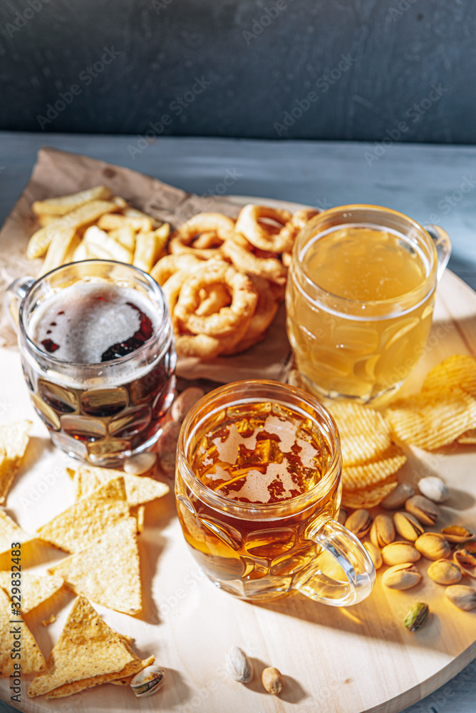 three glasses of expensive craft beer, classic and unfiltered and dark in a glass on the table with a snack of peanut and pistachio chips and nachos