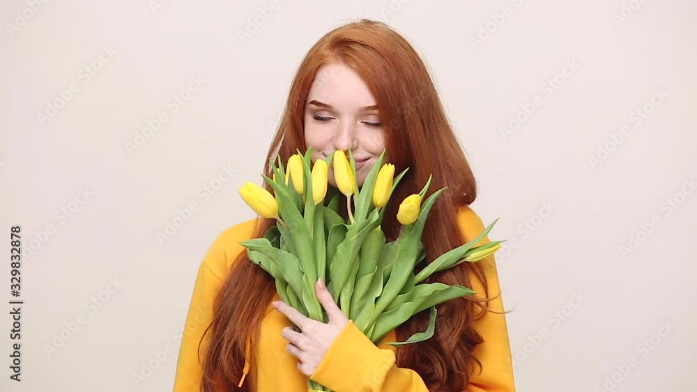 Pretty happy ginger redhead young girl in yellow streetwear hoodie posing isolated on white background in studio. People holiday lifestyle concept. Hold spring flowers tulips feels enjoys floral aroma Pretty happy ginger redhead young girl in yellow streetwear hoodie posing isolated on white background in studio. People holiday lifestyle concept. Hold spring flowers tulips feels enjoys floral aroma