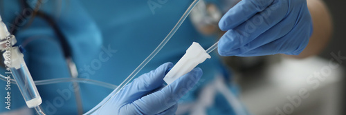 Close-up of female hands in sterile gloves putting dropper to patient. Practitioner wearing medical uniform and stethoscope. Woman standing in clinic ward or procedural. Healthcare and clinic concept