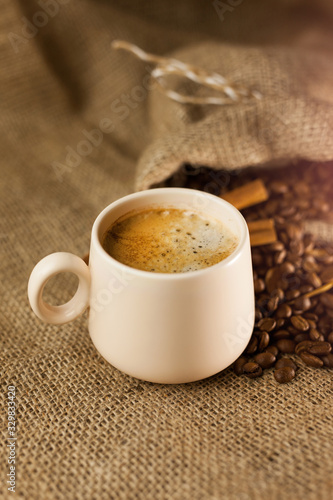 Coffee cup with cinnamon sticks and coffee bag on wooden table