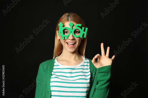 Young woman with party glasses on black background. St. Patrick s Day celebration
