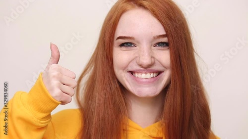 Wallpaper Mural Close up charming ginger redhead curly young girl in yellow streetwear hoodie isolated on white background in studio. People sincere emotions lifestyle concept. Looks at camera showing thumbs up hand Torontodigital.ca